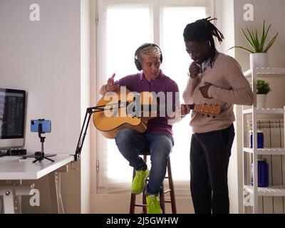 Un tuteur afroamerican personnel explique à son étudiant asiatique comment jouer la corde étudiée correctement. Éducation musicale à la maison Banque D'Images