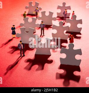 quelques figurines parmi les pièces de puzzle sur une surface rouge Banque D'Images