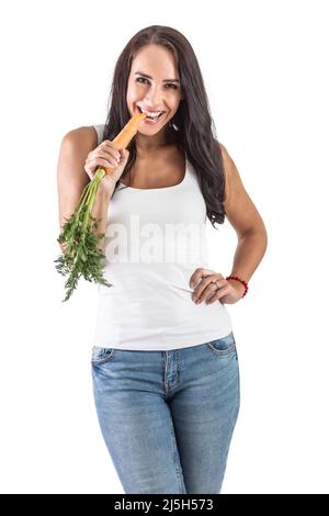 Belle jeune femme mangeant une carotte brute avec un sourire charmant sur un fond blanc. Banque D'Images