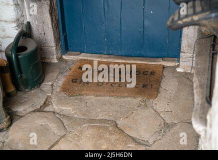 porche d'entrée avec porte bleue et tapis de bienvenue, bottes wellington sur un sol en pierre Banque D'Images