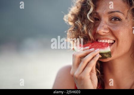 Belle jeune femme aux cheveux bouclés piquant sur la pièce de pastèque. Été, concept de style de vie. Banque D'Images