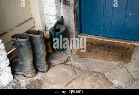 porche d'entrée avec porte bleue et tapis de bienvenue, bottes wellington sur un sol en pierre Banque D'Images