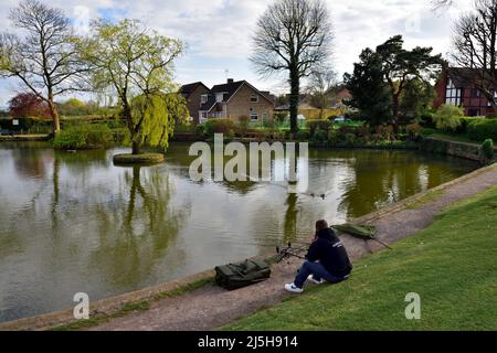 Pêcheur assis à côté de ses cannes à pêche et filet au village de Winterbourne Duck Pond, Bristol, Royaume-Uni Banque D'Images