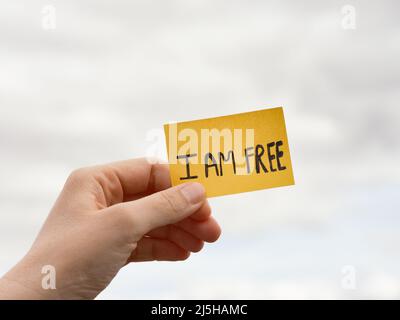 Une femme tenant une note avec les mots que je suis LIBRE sur un fond ciel couvert. Gros plan. Banque D'Images