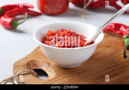 Sauce adjika avec du piment ou de la harissa en pâte dans un bol blanc sur bois Banque D'Images