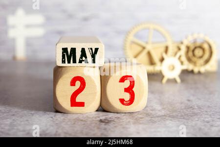 Calendrier pour mai 23: Cube avec le numéro 23, le nom du mois de mai en anglais, arrosoir rose avec un bouquet de crocus pourpre sur un b rose Banque D'Images