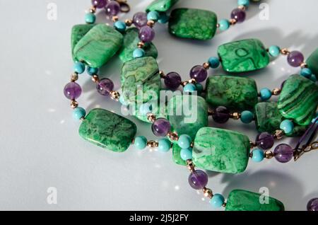 Bobines d'un collier fait à la main avec des perles d'améthyste pourpre, bleu turquoise et vert Crazy agate perles. Vue sur fond blanc avec Drop Banque D'Images