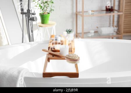 Plateau de bain en bois avec différentes fournitures et produits cosmétiques dans la salle de bains lumineuse Banque D'Images