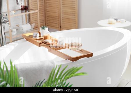 Plateau de bain en bois avec différentes fournitures et produits cosmétiques dans la salle de bains lumineuse Banque D'Images