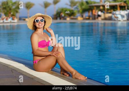 jeune femme souriante dans un chapeau de paille près de la piscine Banque D'Images