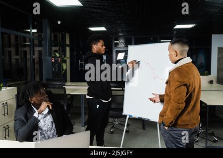 Les crypto-monnaies et les bitcoins sont des discussions graphiques par des investisseurs multiethniques. Les hommes d'affaires d'Afrique noire et d'Asie discutent de la place financière économique Banque D'Images
