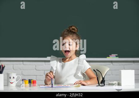 Jolie petite fille enfant peinture avec peinture couleur et pinceau. Leçon de dessin à l'école. Visage amusant pour les enfants. Banque D'Images