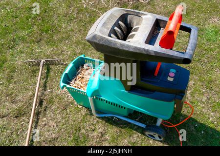 Destructeur de jardin électrique avec pelouse abîmé et pile de branches d'arbre coupées en arrière-plan. Nettoyage autour de la maison. Jardinage de printemps. Élagage Banque D'Images