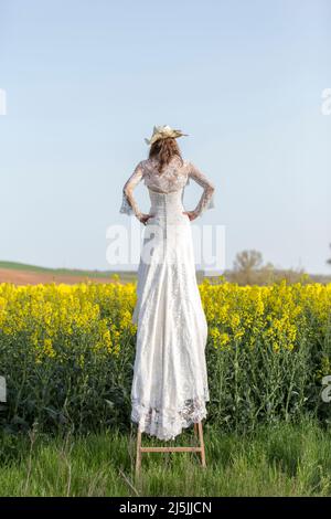 Femme habillée comme une mariée grimpant une échelle au milieu de la nature, entourée par la nature au printemps Banque D'Images