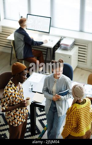Portrait vertical en grand angle de trois jeunes créatifs discutant pendant une pause-café au bureau Banque D'Images