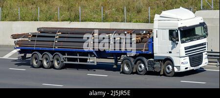 Vue avant et latérale, camion et conducteur DAF hgv blanc sur tracteur avec remorque articulée à plateau chargée de poutres en acier sur autoroute britannique Banque D'Images