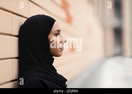 Une jeune athlète islamique sérieuse dans le hijab se penche sur le mur de briques, pense et repose après le jogging Banque D'Images