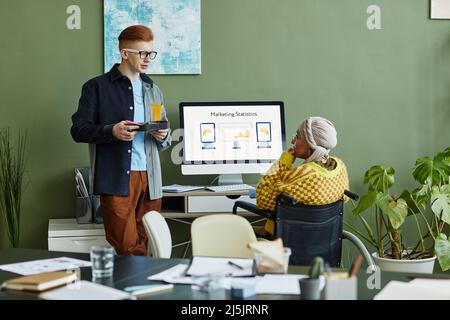 Portrait d'un jeune homme discutant avec une femme en fauteuil roulant au bureau, espace de copie Banque D'Images