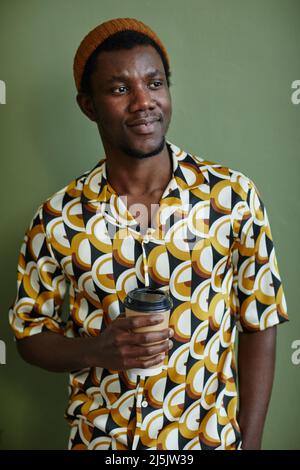 Portrait à la taille du jeune homme noir portant un imprimé tout en se tenant contre le mur vert Banque D'Images