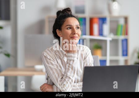 Portrait d'une femme rêveuse de la direction de bureau assise à un bureau, en regardant loin avec un visage plein de plaisir Banque D'Images