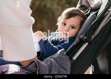 Petit enfant regardant l'appareil photo tout en étant assis dans la poussette à l'extérieur. Banque D'Images