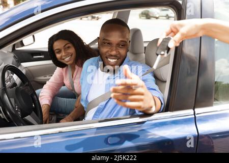 Heureux couple noir assis dans une nouvelle voiture prenant les clés Banque D'Images