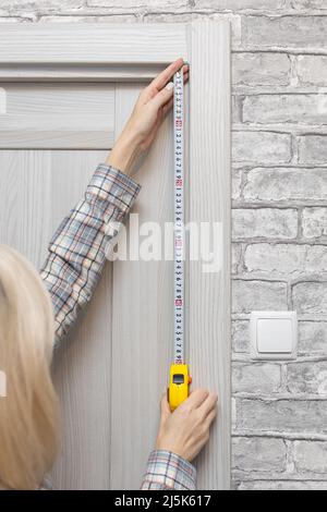 une femme utilisant un mètre à ruban mesure la porte dans l'appartement. Photo de haute qualité Banque D'Images