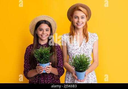 mère et fille sourient avec plante dans pot sur fond jaune Banque D'Images