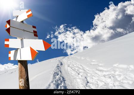 Des panneaux de sentier directionnels vierges dans un magnifique paysage de montagne d'hiver avec de la neige poudreuse et des empreintes de pas contre un ciel bleu clair et des rayons de soleil. Italie. Banque D'Images