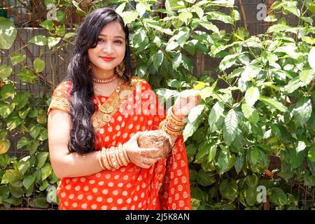 Femme en mekhla rouge tenant l'offrande religieuse, femme indienne en robe traditionnelle sari dans le jardin à la maison Banque D'Images