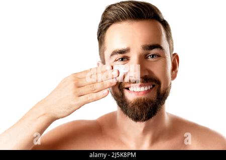 Le jeune homme applique de la crème hydratante et anti-âge sur son visage Banque D'Images