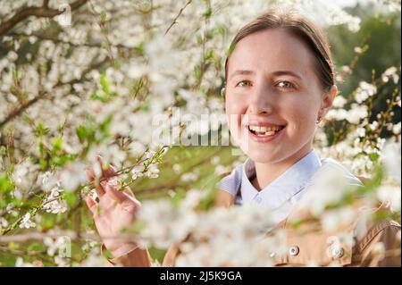 Femme allergique souffrant d'allergies saisonnières au printemps, posant dans un jardin fleuri au printemps. Gros plan femme utilisant le médicament d'allergie parmi les arbres en fleurs. Concept de médicament antihistaminique Banque D'Images