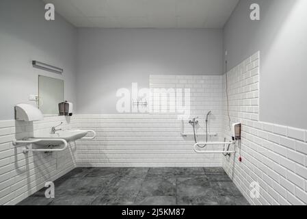 L'intérieur de la salle de bains avec des équipements pour personnes à mobilité réduite. Briques blanches. Carreaux gris. Banque D'Images