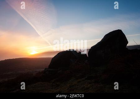 Lever du soleil sur Ilkley Moor avec des rochers silhouettés contre le ciel bleu et les contrailles roses. West Yorkshire, Angleterre, Royaume-Uni Banque D'Images