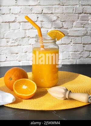 Jus d'orange dans un verre à boire sur un placarat de paille jaune sur un fond de brique blanche Banque D'Images