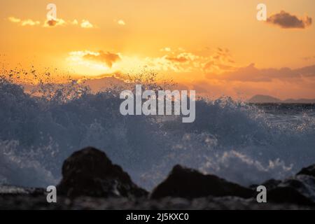 Mer ​​wave au coucher du soleil dans l'heure d'or frappant un rocher sur la plage. Banque D'Images