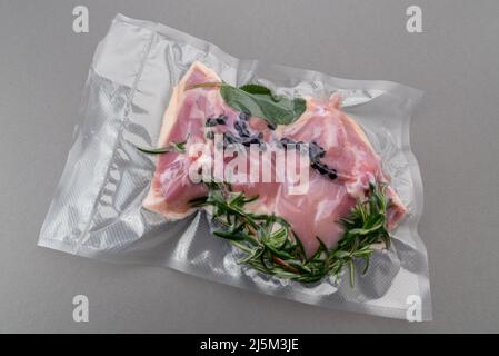 Cuisses de poulet avec sauge au romarin et épices emballées sous vide scellées pour une cuisson sous vide isolée sur fond gris dans la vue de dessus Banque D'Images