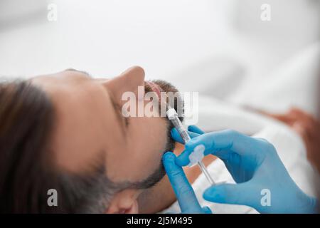 L'homme beau subit une augmentation de la lèvre avec une esthéticienne professionnelle faisant l'injection de soutireuse en clinique Banque D'Images