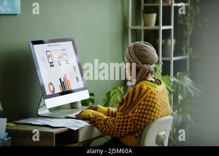 Portrait vibrant de la jeune femme d'affaires ethnique utilisant un ordinateur tout en travaillant à un bureau dans un bureau vert Banque D'Images