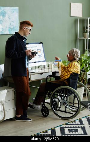Portrait complet d'une jeune femme en fauteuil roulant au bureau et en train de déjeuner avec des collègues Banque D'Images