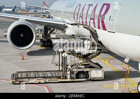 Francfort, Allemagne - avril 2022 : chargeur de fret aérien hydraulique à côté de la soute à ciel ouvert d'un Boeing 777 de Qatar Airways. Banque D'Images