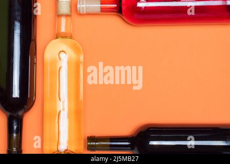 Plusieurs bouteilles de vin, rouge, blanc et rosé, croisées les unes avec les autres, sur fond orange. Banque D'Images