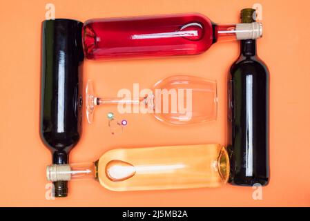 Plusieurs bouteilles de vin, rouge, blanc et rosé, placées horizontalement, croisées les unes avec les autres, avec un verre au milieu. Banque D'Images