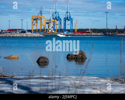 Helsinki / Finlande - 17 AVRIL 2022 : de grandes fleurs de rochers se sont enfuiées de la mer. Rivage recouvert de neige. Vue sur un port de fret en arrière-plan. Banque D'Images