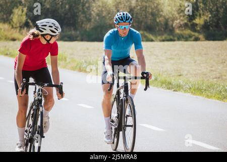 Vue de face d'une femme et d'un homme, des cyclistes professionnels dans les vêtements de sport, en longeant une route asphaltée dans la belle nature verte. Banque D'Images