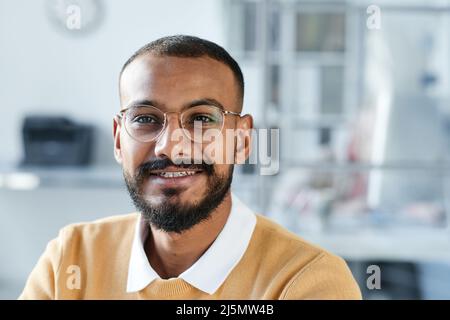 Portrait souriant jeune directeur de course mixte en lunettes assis dans un bureau contemporain Banque D'Images