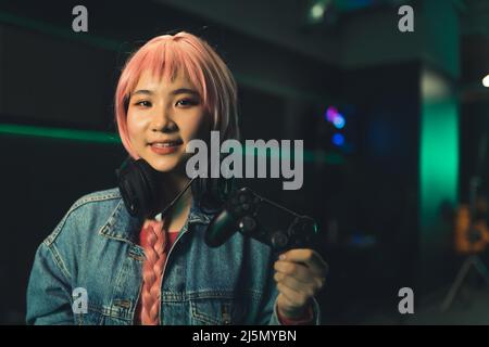 Jeune femme asiatique attrayante porte des écouteurs et tient joystick arrière-plan sombre portrait copie espace . Photo de haute qualité Banque D'Images
