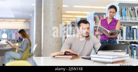 Guy étudiant se préparant à un examen sur un ordinateur portable dans la bibliothèque Banque D'Images