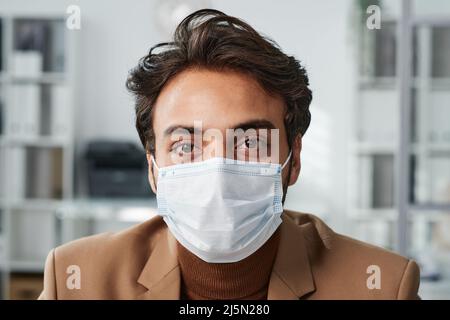 Portrait d'un beau jeune directeur du Moyen-Orient en masque assis dans un bureau contemporain Banque D'Images
