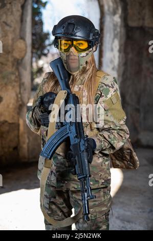 Portrait d'une femme dans un casque et des lunettes avec une mitrailleuse dans les mains. Une femme soldat en uniforme de camouflage tient une arme. Banque D'Images